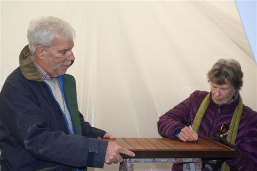Carol Stephens signing wood interior plank of Dorade with Matt Brooks watching.