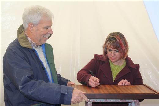 Marcy Stephens signing wood interior plank of Dorade with Matt Brooks watching.